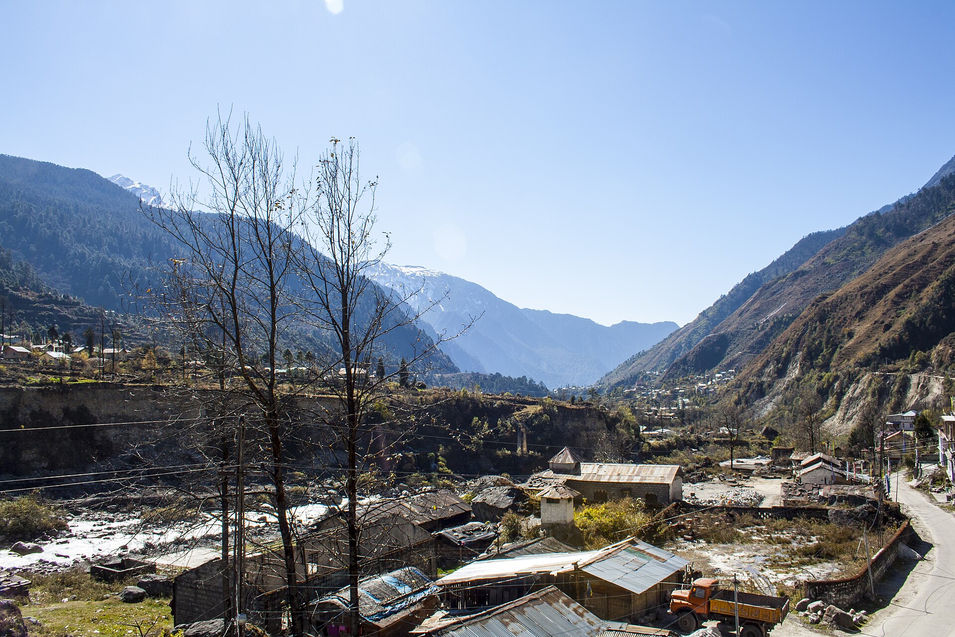 Mountain road and houses in Lachung beside a river in a steep valley under a clear blue sky